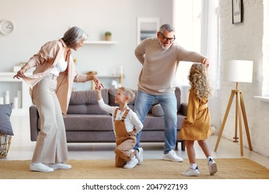 Active Senior Grandparents Dancing With Two Happy Kids Grandchildren In Living Room, Small Children Sister And Brother Having Fun In Living Room While Playing With Grand Mother And Grandfather