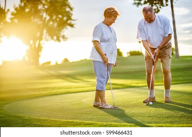 Active Senior Lifestyle, Elderly Couple Playing Golf Together At Sunset