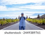 Active senior man with backpack walking in mountain road looking at camera with thumb up, La Gomera island at horizon over sea, retired senior enjoys freedom and travel in Tenerife canary islands