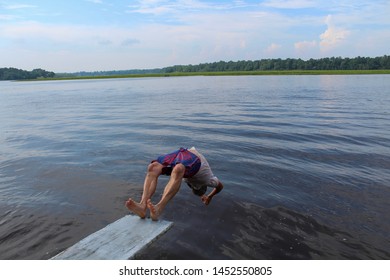 Active Senior Man Doing Back Dive Off A Diving Board Over River