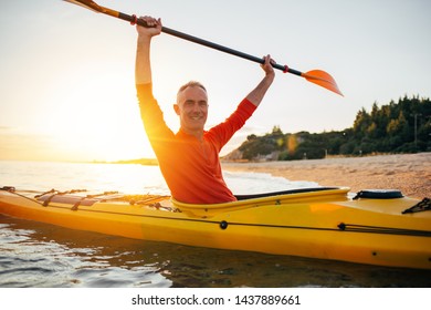 Active Senior Man Enjoy Paddling Kayak On The Sunset Sea. Smiling Middle Aged Man Holding Kayak Paddles High