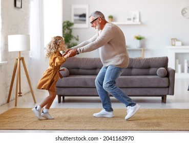 Active senior man grandfather enjoying dance with cute little granddaughter in stylish living room at home, small adorable girl in dress dancing with grandpa while spending time together on weekend - Shutterstock ID 2041162970