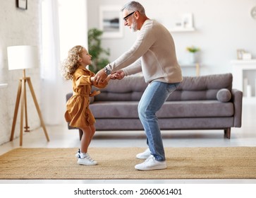 Active Senior Man Grandfather Enjoying Dance With Cute Little Granddaughter In Stylish Living Room At Home, Small Adorable Girl In Dress Dancing With Grandpa While Spending Time Together On Weekend