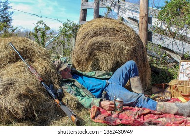 Active Senior Man Hunter Relaxing Against Hay Bale With Shotgun And Beer Stein