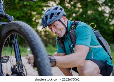 Active senior man repairing bicycle, pumping up tire in nature in summer.