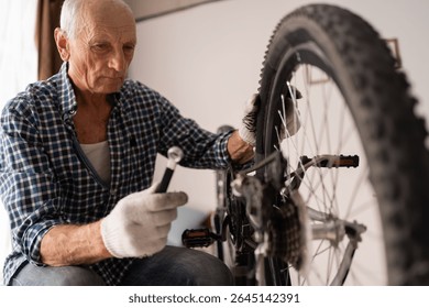 Active senior man repairing bicycle at home. cycling leisure. Retired male home mechanic with equipment for bike maintenance fixing wheel with wrench