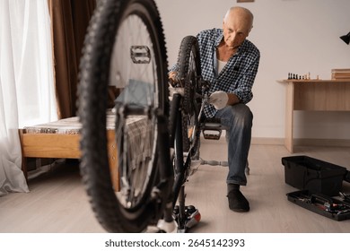 Active senior man repairing bicycle at home. cycling leisure. Retired male home mechanic with equipment for bike maintenance fixing wheel with wrench. Close-up