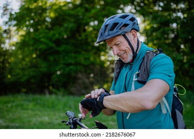 Active senior man riding bicycle at summer park, looking at smartwatch and checking his performance, healthy lifestyle concept. - Powered by Shutterstock