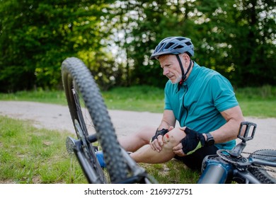 Active senior man in sportswear fell off bicycle on the ground and injured his knee, in park in summer.