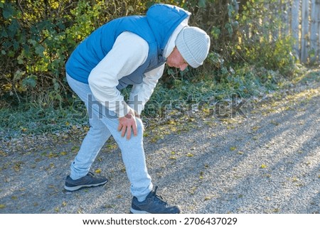 active senior man stops during winter run holding knee after sudden discomfort, jogging, running challenge, health awareness, exercise caution, unexpected pause, outdoor fitness, active lifestyle