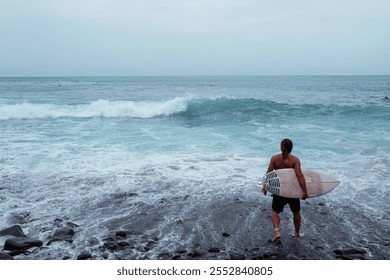 Active senior surfer walking on rocky beach, holding surfboard and getting ready to surf ocean waves - Powered by Shutterstock