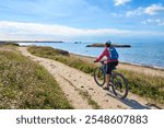 active senior woman cycling with her electric mountain bike at the wild coast of Quiberon peninsula, Brittany, France
