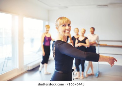Active Senior Woman Doing Ballet In A Dance Studio With A Group Of Friends In The Background