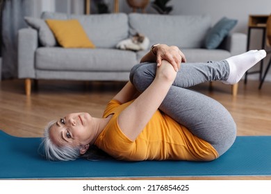 Active Senior Woman Doing Exercises On Yoga Mat, Working Out At Home, Relaxing Her Back Muscles, Looking And Smiling At Camera During Domestic Training