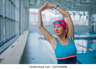 Active Senior Woman Doing Warming Up Exercise Indoors In Public Swimming Pool.