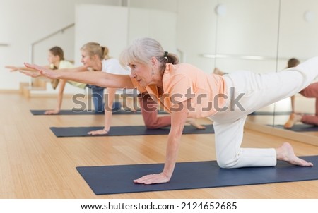 Active senior woman exercising stretching workout and incline during yoga class in fitness studio