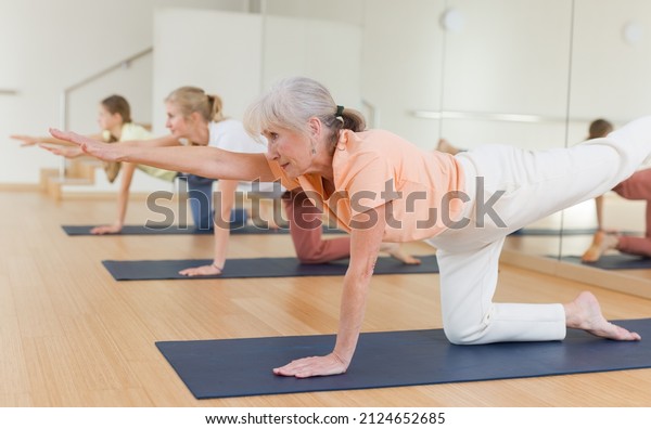 Active senior woman exercising\
stretching workout and incline during yoga class in fitness\
studio