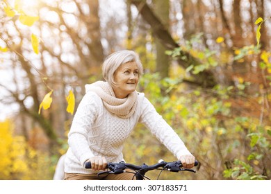 Active Senior Woman Riding Bike In Autumn Nature. 
