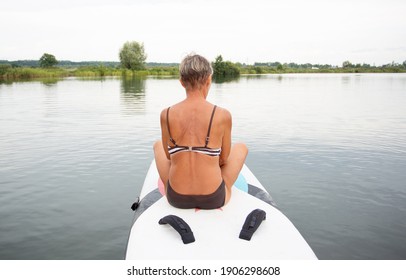 Active Senior Woman In Swim Suit Sitting On Surf In The Water 