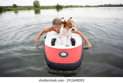 Active Senior Woman In Swim Suit Lying On Surf With Dog In The Water 