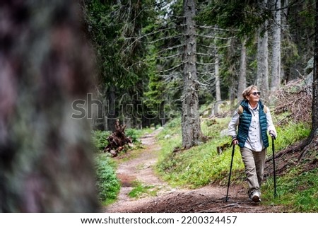 Active senior woman walking with Nordic poles while enjoying hike in beautiful autumn forest