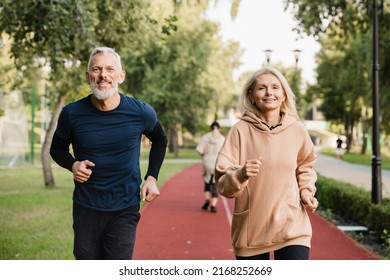 Active seniors. Caucasian mature couple running jogging together, doing slimming exercises in fitness clothes in stadium in the morning. - Powered by Shutterstock