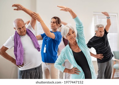 Active seniors doing exercise with physiotherapist at nursing home gym. Trainer helping elderly man and old woman exercising at home. Retired people doing stretching exercises at retirement community.