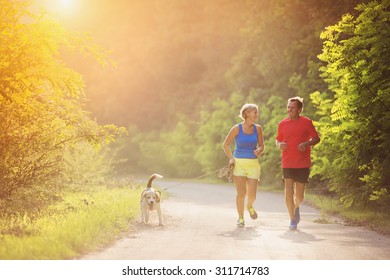 Active Seniors Running With Their Dog Outside In Green Nature