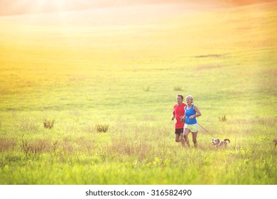 Active Seniors Running With Their Dog Outside In Green Nature