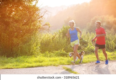 Active Seniors Running With Their Dog Outside In Green Nature