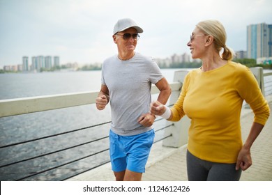 Active seniors in sunglasses jogging along riverside in urban environment