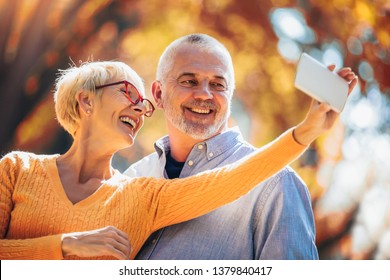 Active seniors taking selfies of them having fun outside in the autumn forest - Powered by Shutterstock