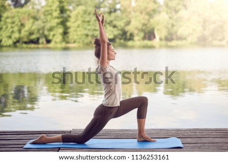 Active slim young woman doing yoga by the lake