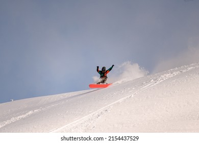 active snowboarder in bright overalls slides down the mountain on splitboard on powdery snow. Ski touring in mountains, winter freeride extreme sport.