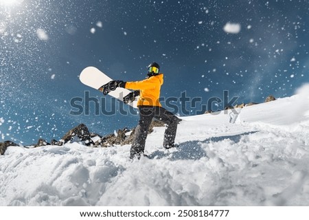 Active snowboarder is having fun and breaks snowball with snowboard. Powder snow flies around snowboarder