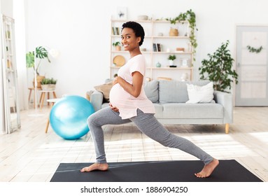 Active and sportive pregnancy concept. Cheerful pregnant black woman doing lunges, stretching her legs, exercising at home. Healthy African American expectant lady training in living room