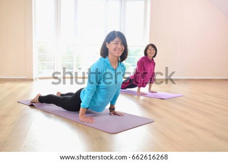 Active sportive women doing handstand exercise practicing the plank pose during yoga class in a gym. Two women doing stretching exercises and practicing yoga in studio with big windows on background