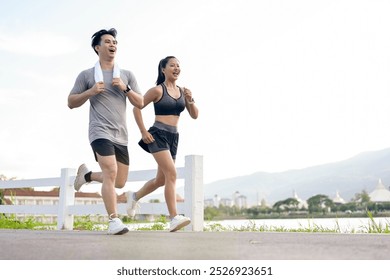 An active, sporty Asian couple in sportswear is jogging or running together in the park in the morning. girlfriend and boyfriend, healthy lifestyle, workout, outdoor activity - Powered by Shutterstock