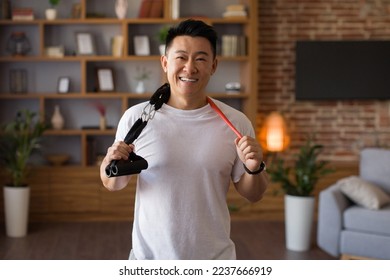 Active sporty lifestyle. Excited japanese middle aged man holding trx resistance bands hang around his neck, standing in living room and posing to camera - Powered by Shutterstock