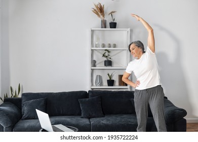 Active And Sporty Senior Female Warming Out Before Workout At Home, An Older Woman Stretching Arms In Front Of The Laptop, A Middle Aged Lady Exercising With Video Tutorial. Healthy Lifestyle Concept