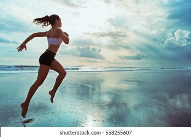 Active sporty woman run along ocean surf by water pool to keep fit and health. Sunset black sand beach background with sun. Woman fitness, jogging workout and sport activity on summer family holiday.