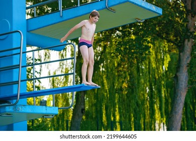 Active Teenager Boy Jumping Into An Outdoor Pool From Spring Board Or 5 Meters Diving Tower Learning To Dive During Sport Class On A Hot Summer Day. Happy Brave Child.