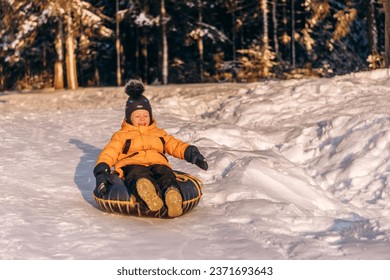 Active toddler boy in a yellow jacket sliding down the hill on snow tube.Winter fun,active lifestyle concept.