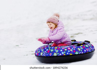 Active Toddler Girl Sliding Down The Hill On Snow Tube. Cute Little Happy Child Having Fun Outdoors In Winter On Sledge . Healthy Excited Kid Tubing Snowy Downhill, Family Winter Time.