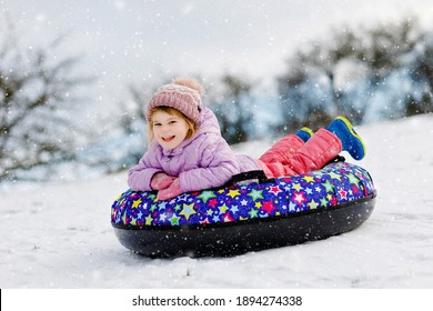 Active Toddler Girl Sliding Down The Hill On Snow Tube. Cute Little Happy Child Having Fun Outdoors In Winter On Sledge . Healthy Excited Kid Tubing Snowy Downhill, Family Winter Time.