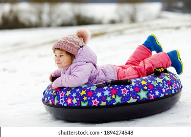 Active Toddler Girl Sliding Down The Hill On Snow Tube. Cute Little Happy Child Having Fun Outdoors In Winter On Sledge . Healthy Excited Kid Tubing Snowy Downhill, Family Winter Time.