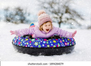 Active Toddler Girl Sliding Down The Hill On Snow Tube. Cute Little Happy Child Having Fun Outdoors In Winter On Sledge . Healthy Excited Kid Tubing Snowy Downhill, Family Winter Time.