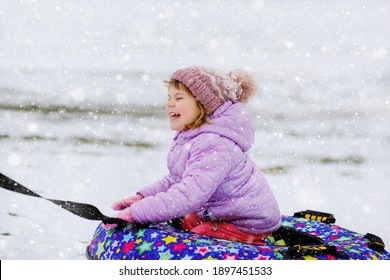 Active Toddler Girl Sliding Down The Hill On Snow Tube. Cute Little Happy Child Having Fun Outdoors In Winter On Sledge . Healthy Excited Kid Tubing Snowy Downhill, Family Winter Time.