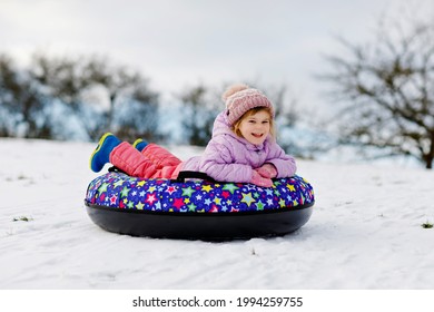 Active Toddler Girl Sliding Down The Hill On Snow Tube. Cute Little Happy Child Having Fun Outdoors In Winter On Sledge . Healthy Excited Kid Tubing Snowy Downhill, Family Winter Time.