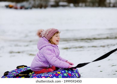 Active Toddler Girl Sliding Down The Hill On Snow Tube. Cute Little Happy Child Having Fun Outdoors In Winter On Sledge . Healthy Excited Kid Tubing Snowy Downhill, Family Winter Time.